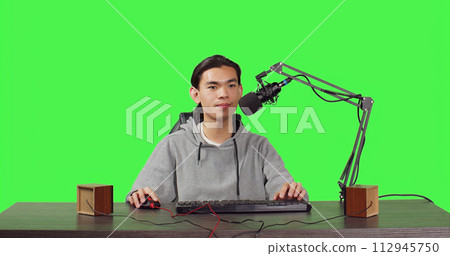 POV of vlogger broadcasting rpg gameplay over full body greenscreen in studio, content creator streaming live web contest. Asian video blogger playing games and broadcasting at desk. 112945750