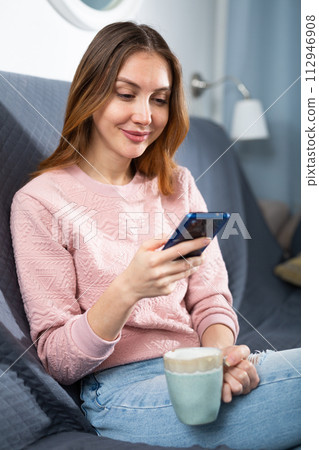 Young woman sitting on couch and texting message with her smartphone Young woman sitting on couch and texting message with her smartphone 112946908