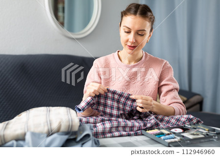 Woman repairing clothes with a needle and thread Woman repairing clothes with a needle and thread 112946960