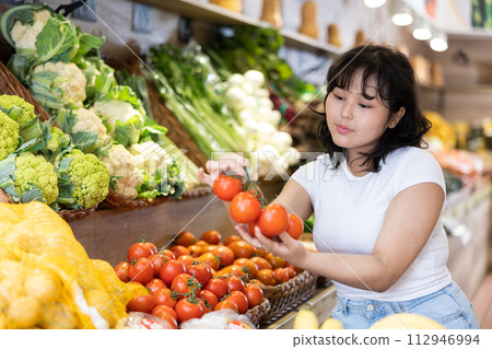 Portrait of positive satisfied girl buying tomatoes in grocery shop 112946994