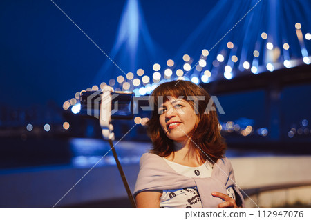 A girl takes pictures of herself on her phone at night in the city A girl takes pictures of herself on her phone at night in the city 112947076