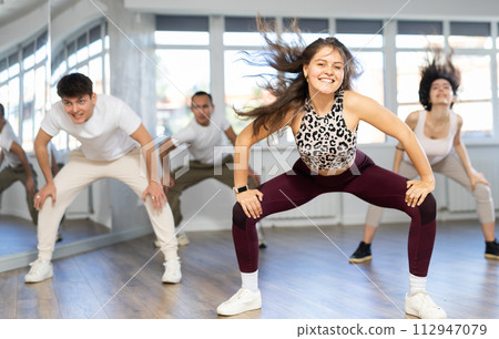 Happy emotional young female dancer rehearsing popping techniques during group workout in modern street dance studio 112947079