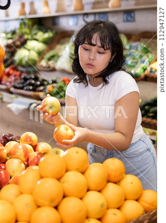 Happy smiling girl making purchases in supermarket, choosing fresh apples 112947127