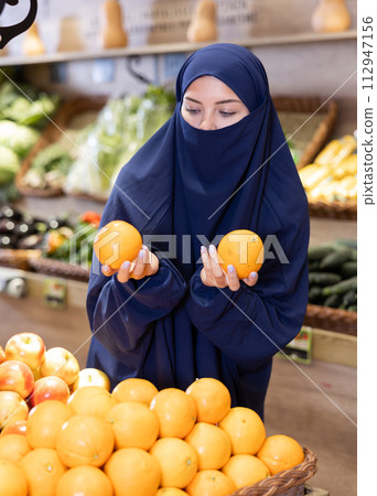 Young Muslim woman in niqab choosing oranges in supermarket Young Muslim woman in niqab choosing oranges in supermarket 112947156
