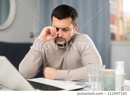 Man rubs tired eyes with his hands after a long work at laptop at home 112947165