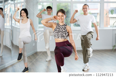 Positive young woman dancing modern dance with other people during group training Positive young woman dancing modern dance with other people during group training 112947213