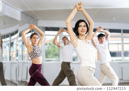 Young sports girl rehearsing modern dances during group training in dance studio 112947215