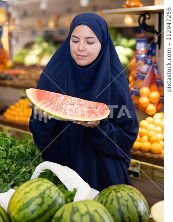 Young woman in muslim dress choosing watermelon at fruit market 112947256