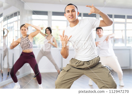 Positive young men and girls dancing modern street dance together during their group training at dance hall Positive young men and girls dancing modern street dance together during their group training at dance hall 112947270