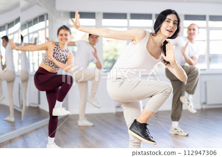 Happy girl and group of young active sport people practicing vogue dancing movements while training twist or charleston in dance hall 112947306