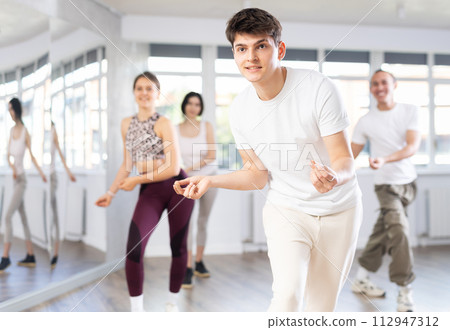 Group of happy young people enjoying a contemporary dancing class. Team of smiling dancers in casual wear practising new choreo 112947312