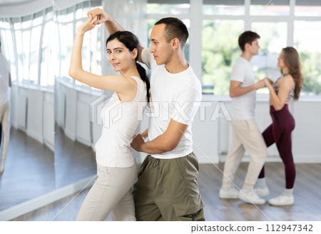 Happy young woman enjoying training dancing active swing with male partner in dance room. Social dancing concept 112947342