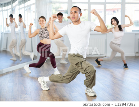 Positive smiling young man dancing hip hop with group of guys and girls in dance class 112947382