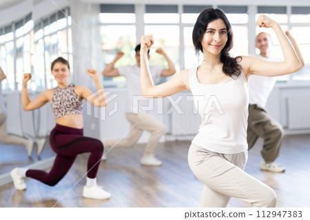 Positive woman and man engaged in dancing in group practices energetic swing in dance studio 112947383