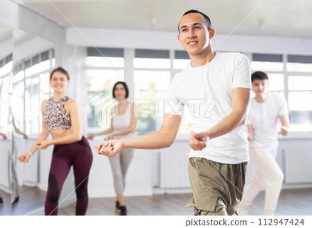Group of happy young people enjoying a contemporary dancing class. Team of smiling dancers in casual wear practising new choreo 112947424