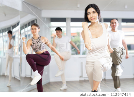 Young happy sports girl rehearsing vigorous swing during group training in dance studio Young happy sports girl rehearsing vigorous swing during group training in dance studio 112947434