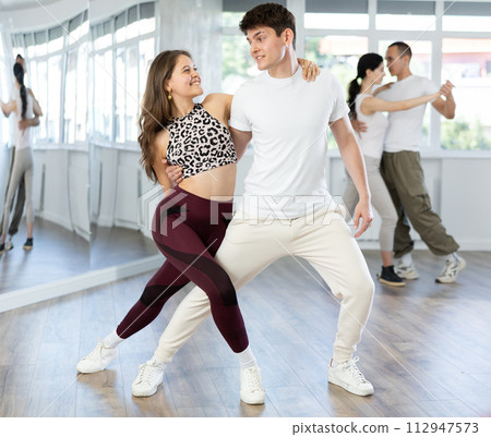 Smiling young woman in sports clothes learn to dance couples latin dance, energetic and fast tango in dance salon 112947573