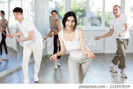 Girl enjoys active dancing, learns new movements, moves synchronously with participants of lesson Girl enjoys active dancing, learns new movements, moves synchronously with participants of lesson 112947634