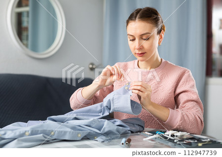 Young woman sewing on button at home 112947739