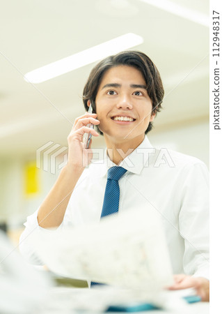一個年輕的商人在辦公室打電話 112948317