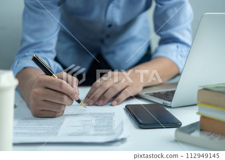 Male hand holding a pen to write a document or sign a business or legal contract. Checklist of financial documents and market reports 112949145