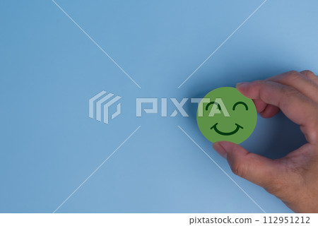 customer service evaluation and satisfaction survey concept. hand holding emotion happy smile face icon on wooden cube on blue background. copy space customer service evaluation and satisfaction survey concept. hand holding emotion happy smile face icon on wooden cube on blue background. copy space 112951212