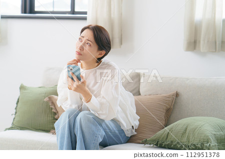 A woman sitting on a sofa with a smartphone 112951378