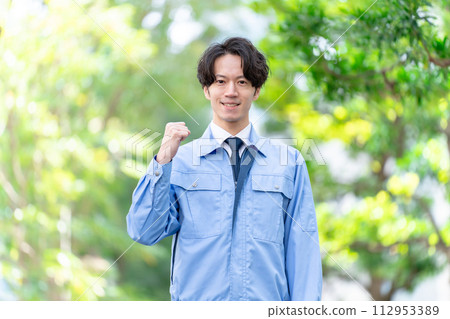 Man in work clothes outdoors, fresh greenery, fist pump 112953389
