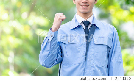 Man in work clothes outdoors, fresh greenery, fist pump 112953390