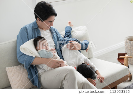 一位年輕的父親在度假時在客廳照顧他的兄弟姐妹。祝你好運！爸爸 112953535