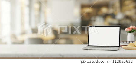 A white-screen laptop computer mockup on a wooden table in a contemporary cosy coffee shop. 112953632