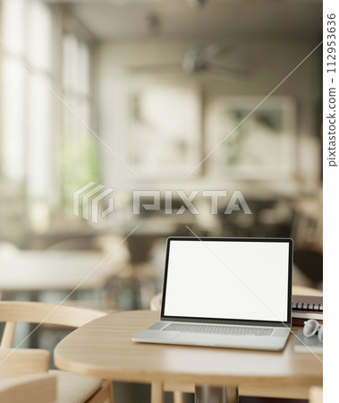 A modern, minimalist coffee shop features a white screen laptop computer mockup on a wooden table. 112953636