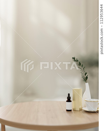 A round wooden tabletop with a serum bottle and a space for display products in a white room. A round wooden tabletop with a serum bottle and a space for display products in a white room. 112953644