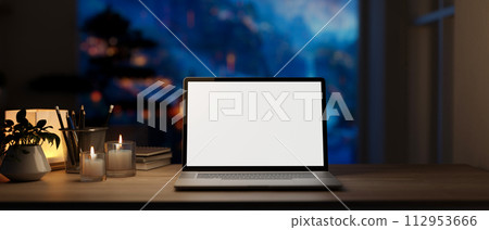 Home workspace at night features a white-screen laptop computer mockup on a wooden desk. Home workspace at night features a white-screen laptop computer mockup on a wooden desk. 112953666