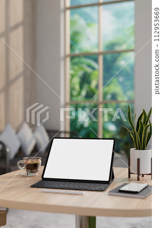A white-screen digital tablet and accessories on a wooden table in a contemporary living room. 112953669