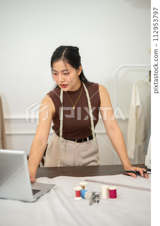 A professional, confident Asian female fashion designer is working in her studio. A professional, confident Asian female fashion designer is working in her studio. 112953797
