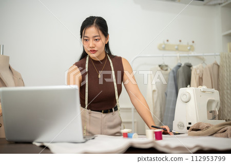 A professional, confident Asian female fashion designer is working in her studio. A professional, confident Asian female fashion designer is working in her studio. 112953799