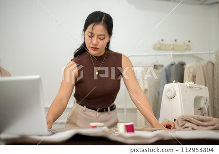A professional Asian female fashion designer or tailor is focusing on her work in the atelier studio 112953804