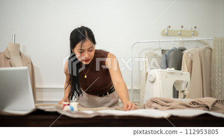 A professional Asian female fashion designer or tailor is focusing on her work in the atelier studio 112953805