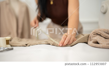 A close-up shot of a professional female fashion designer is measuring fabric with a measuring tape. A close-up shot of a professional female fashion designer is measuring fabric with a measuring tape. 112953807