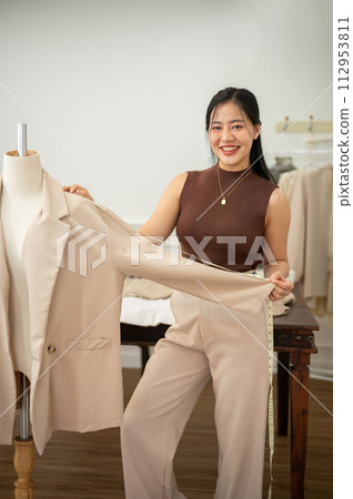 An attractive female tailor is working in her studio, checking her suit pattern on a tailor dummy. 112953811