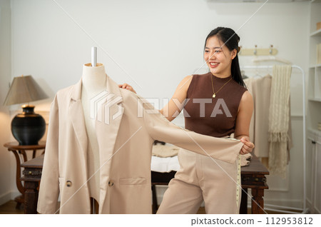 An attractive female tailor is working in her studio, checking her suit pattern on a tailor dummy. An attractive female tailor is working in her studio, checking her suit pattern on a tailor dummy. 112953812