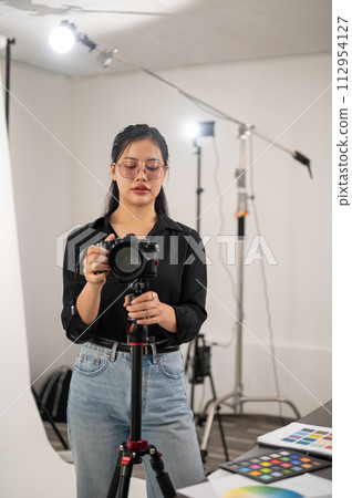A professional Asian female photographer is adjusting her DSLR camera on a tripod stand. A professional Asian female photographer is adjusting her DSLR camera on a tripod stand. 112954127