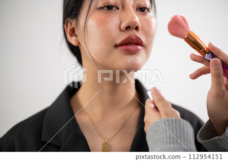 A female model is having makeup applied by a makeup artist, preparing for a photoshoot in the studio A female model is having makeup applied by a makeup artist, preparing for a photoshoot in the studio 112954151