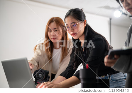 A professional Asian female photographer is working with her assistants in a photoshoot studio. A professional Asian female photographer is working with her assistants in a photoshoot studio. 112954243