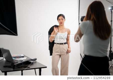 A professional photographer is taking pictures of an attractive young Asian female model in a studio A professional photographer is taking pictures of an attractive young Asian female model in a studio 112954289