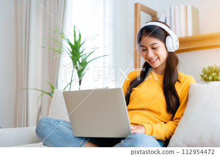 Young adorable asian woman smile wearing headset working in living room at home Young adorable asian woman smile wearing headset working in living room at home 112954472