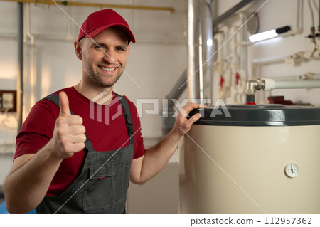 Professional Plumber Inspecting a Water Heater in a Residential Utility Room 112957362