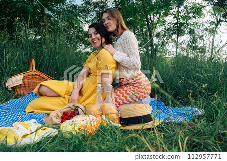 Two girls on a date sit on a blue blanket for a picnic in nature Two girls on a date sit on a blue blanket for a picnic in nature 112957771