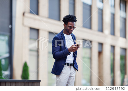 Stylish African American man in smart casual clothes, with mobile phone against backdrop of city. Fashionable guy with smartphone outdoors Stylish African American man in smart casual clothes, with mobile phone against backdrop of city. Fashionable guy with smartphone outdoors 112958592